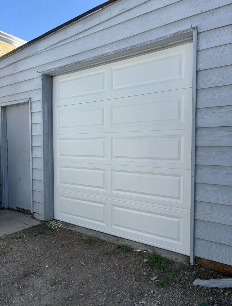 White raised-panel single-car garage door on a gray-sided garage