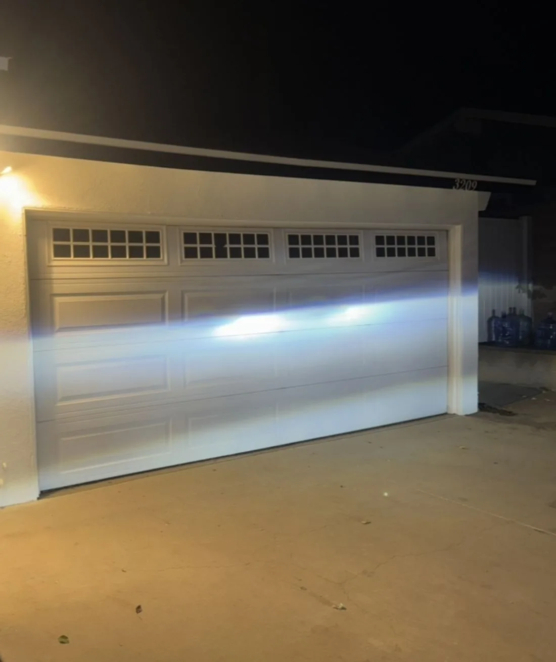 Finished white raised-panel double garage door with a row of windows, lit at night